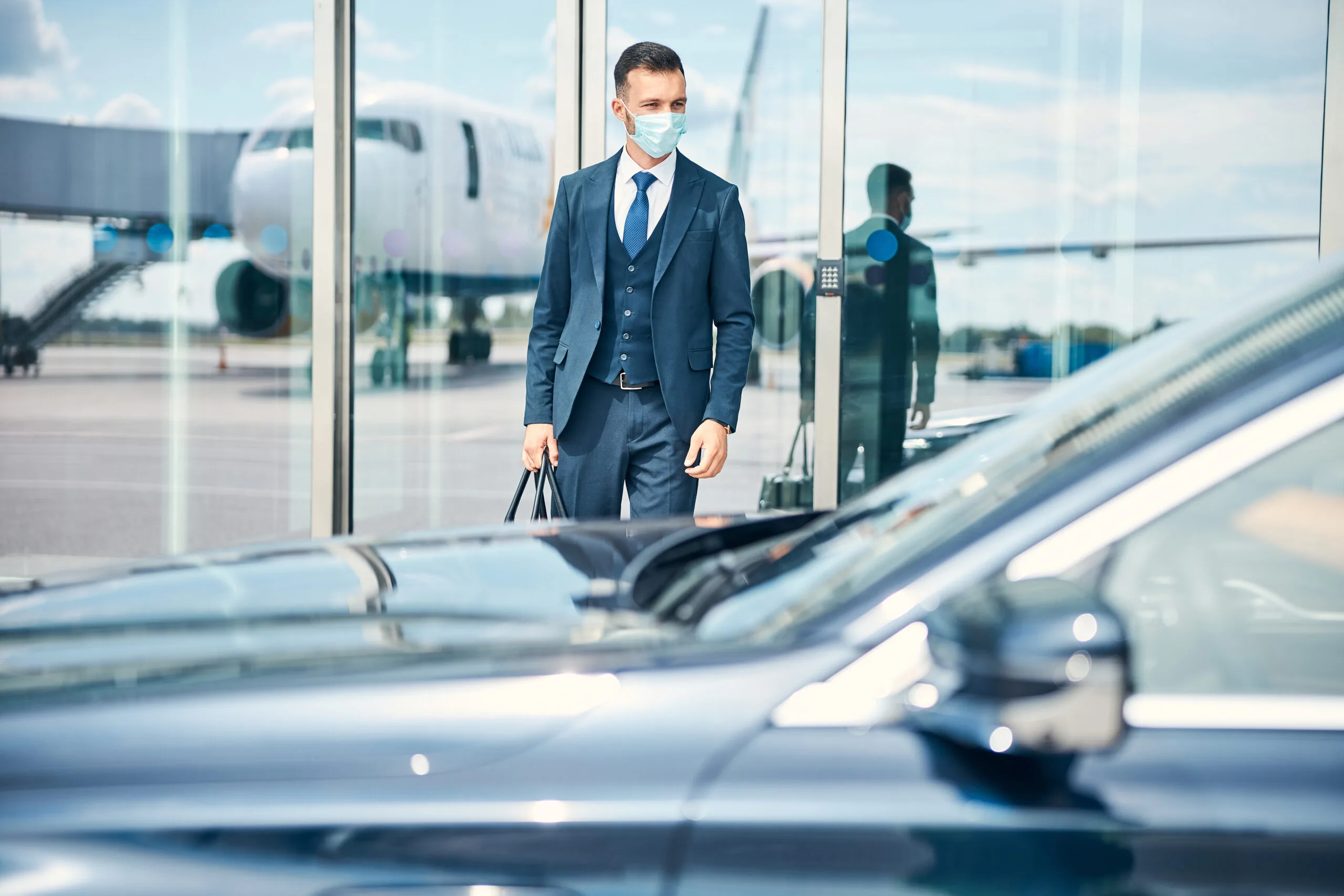 businessman with bag hand standing near glass door airport looking car front him medical mask his fa